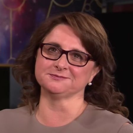 Victoria Alonso is wearing glasses and a grey dress in the picture.